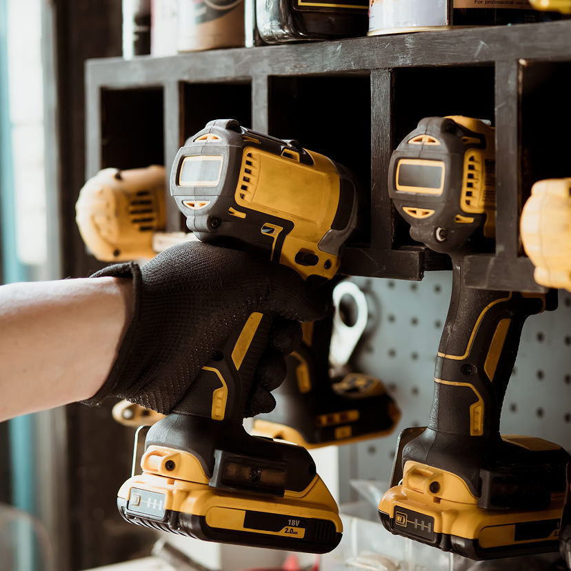 Person holding a cordless drill with a pegboard of tools in the background